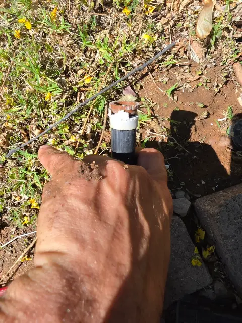 Hand holding a sprinkler head being fitted next to a shrub